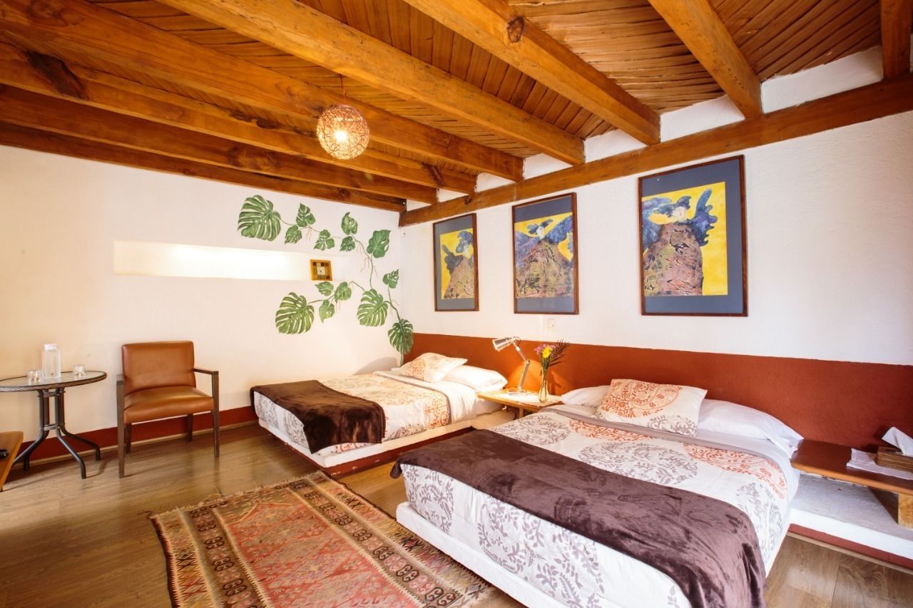 A room with two beds, a small table, a chair, and a decorative plant wall.