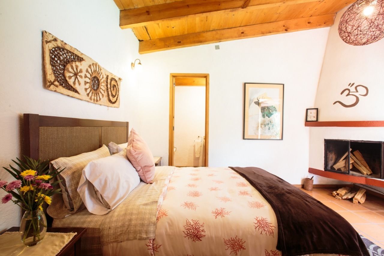 A bedroom with a bed, a wooden headboard, a wall-mounted artwork, a framed picture, a fireplace, and a door.