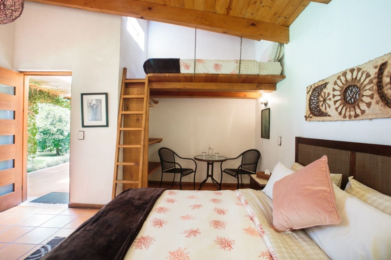 A bedroom with a bunk bed, a small table with chairs, a ladder, and a view of the garden.