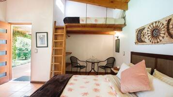 A bedroom with a bunk bed, a small table with chairs, a ladder, and a view of the garden.