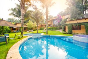 A swimming pool with lounge chairs and umbrellas, surrounded by greenery and buildings. - Hotel La Joya del Viento (Valle de Bravo)