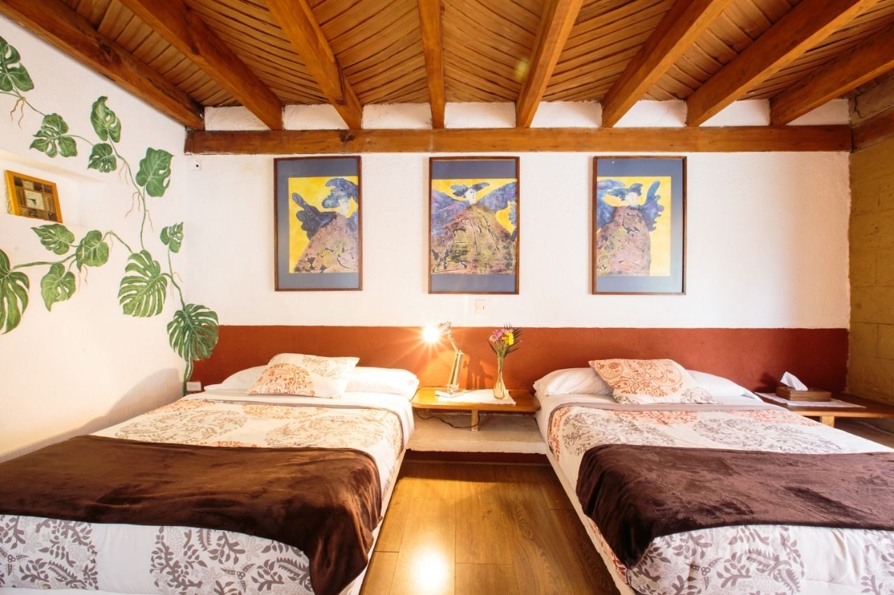 A room with two beds, wooden beams on the ceiling, and three framed paintings on the wall.