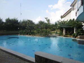 A swimming pool with a stone border, surrounded by tropical plants and a clear sky.