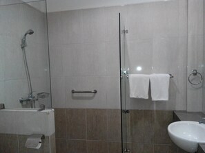 Un baño moderno con cabina de ducha de vidrio, un perchero con dos toallas, un lavamanos y un inodoro.