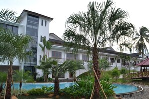 A modern hotel with a swimming pool surrounded by palm trees and lush greenery.