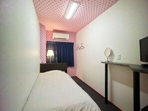 Ett hotellrum med en säng, ett skrivbord med en spegel, en TV, en luftkonditionering och ett fönster med gardiner.