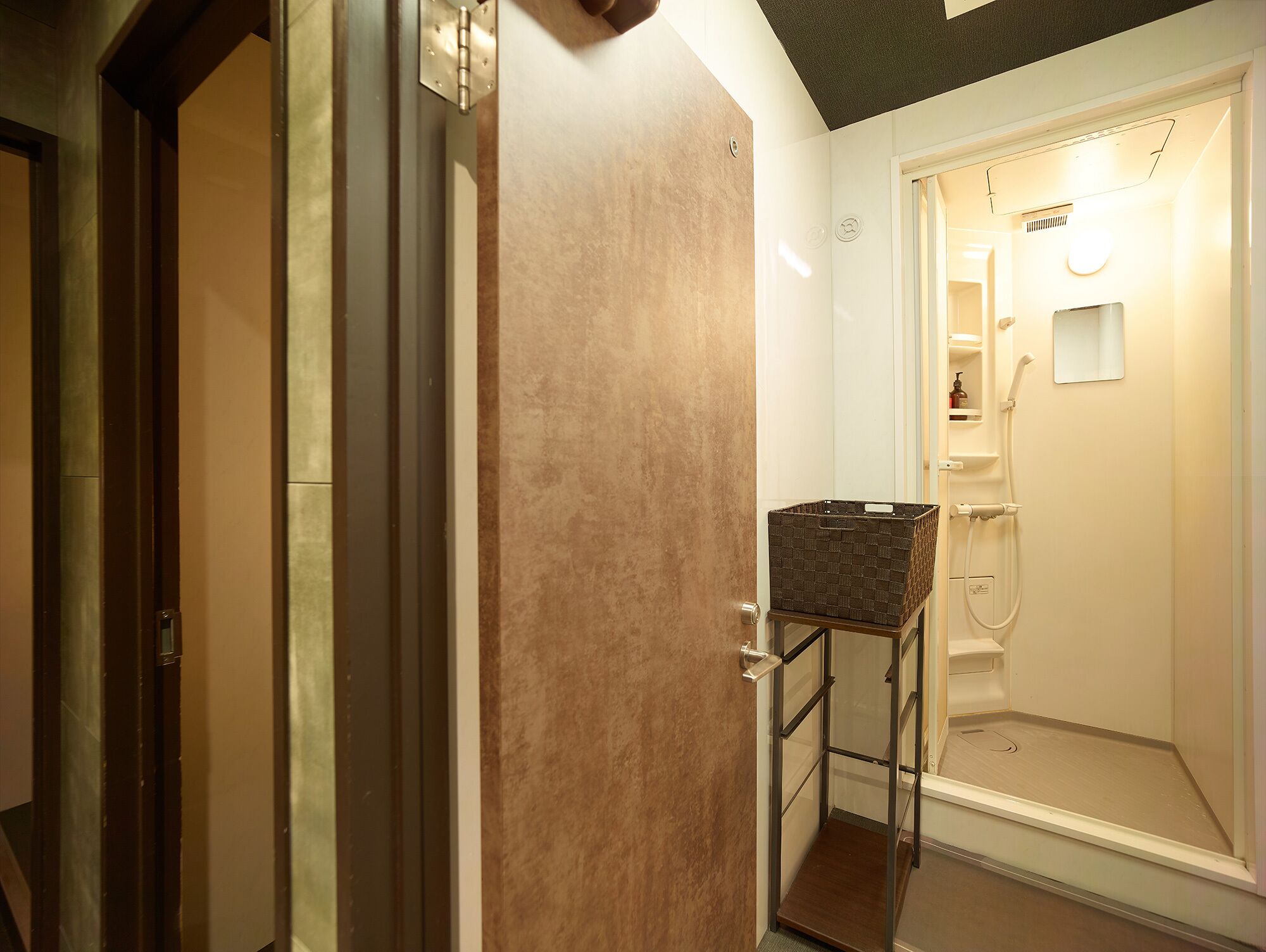 Une salle de bain moderne avec une douche à l’italienne, une petite étagère pour les articles de toilette et un panier posé sur un support en métal.