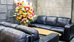 Um lobby moderno com sofás de couro preto, uma mesa de centro de madeira e um grande arranjo de flores.