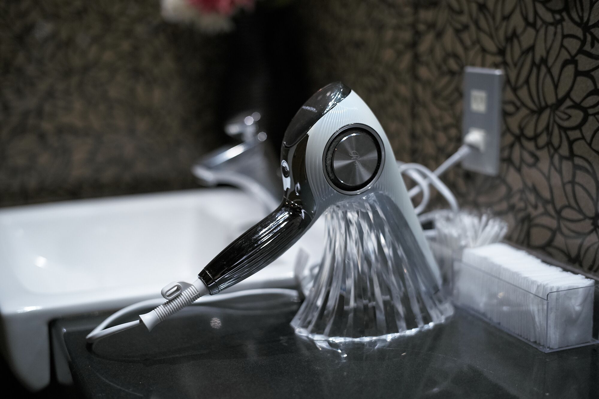 Un baño con un grifo moderno, un recipiente de vidrio transparente y un lavamanos blanco.