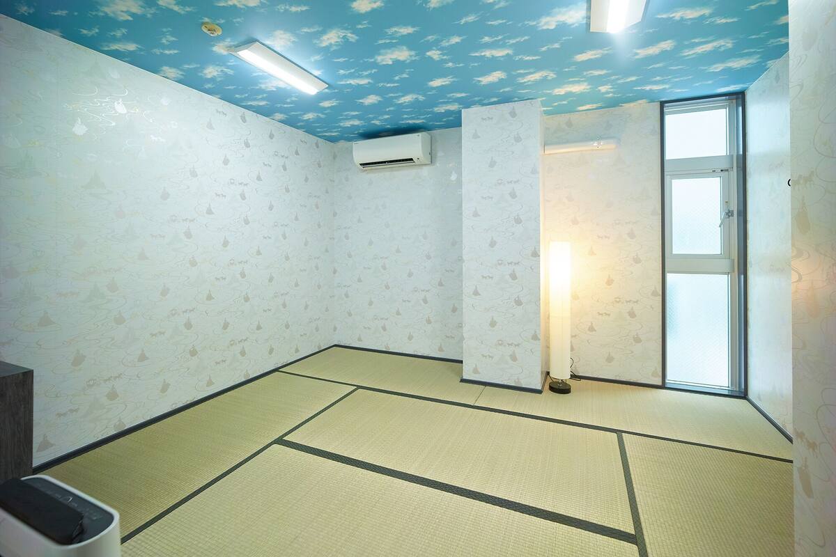 Ein Zimmer mit Tatami-Boden, einer Decke mit Wolkenmuster, einer Klimaanlage und einem Fenster mit Blick.