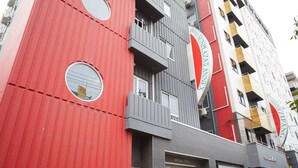 Um hotel com fachada vermelha, várias varandas e uma máquina de refrigerantes Coca-Cola.