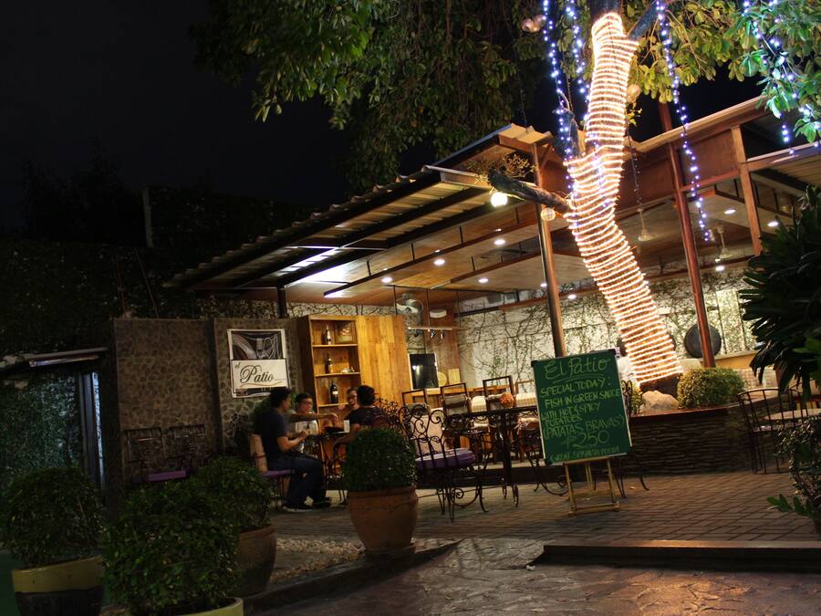 An outdoor dining area with tables and chairs, a signboard, and decorative lights.