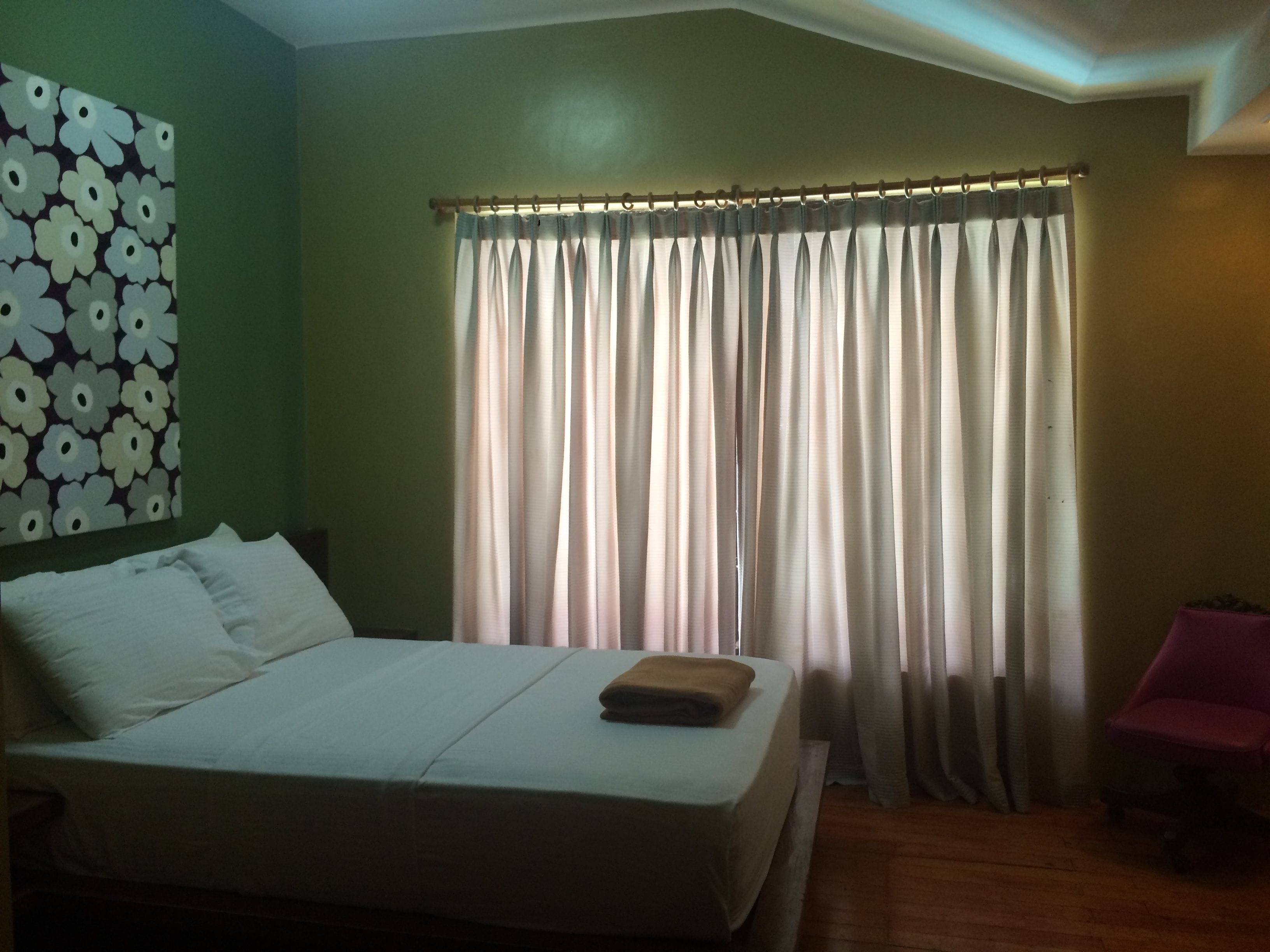 A hotel room with a bed, a chair, a curtain, and a wall with a floral pattern.