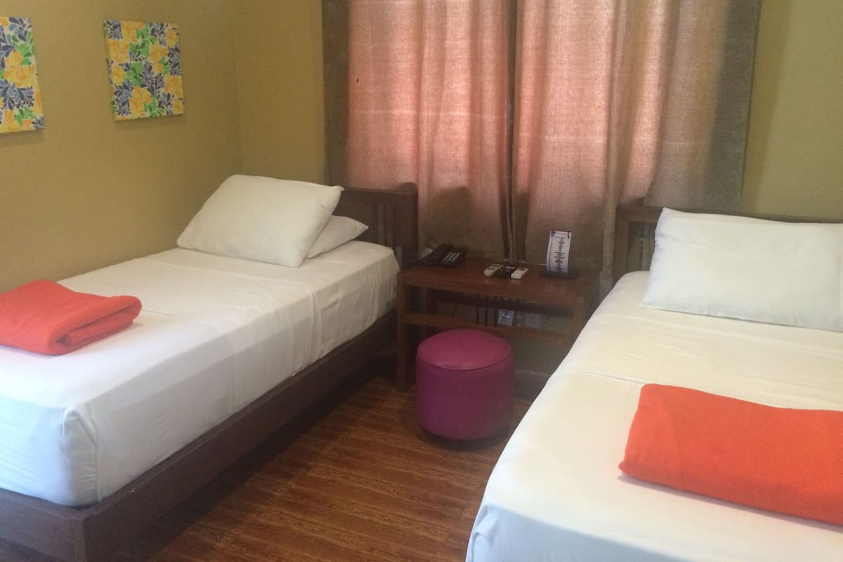 Quarto de hotel com duas camas de solteiro, uma mesa de cabeceira de madeira, um telefone e uma pequena mesa com abajur.
