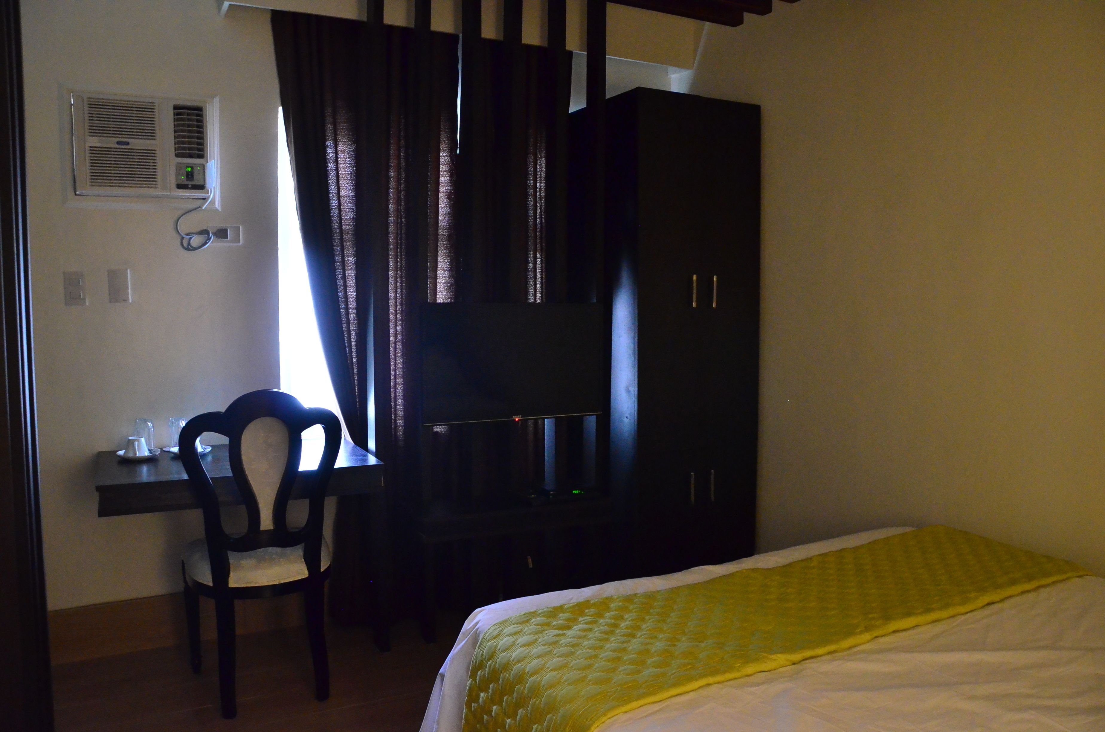 Habitación de hotel con cama, escritorio, silla, armario y ventana con cortinas.