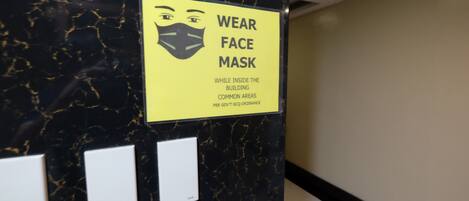 A sign instructing to wear a face mask in common areas, mounted on a black marble wall with three switches below it.