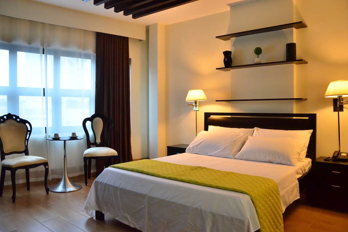 Une chambre d’hôtel avec un lit, deux chaises, une petite table et une lampe.