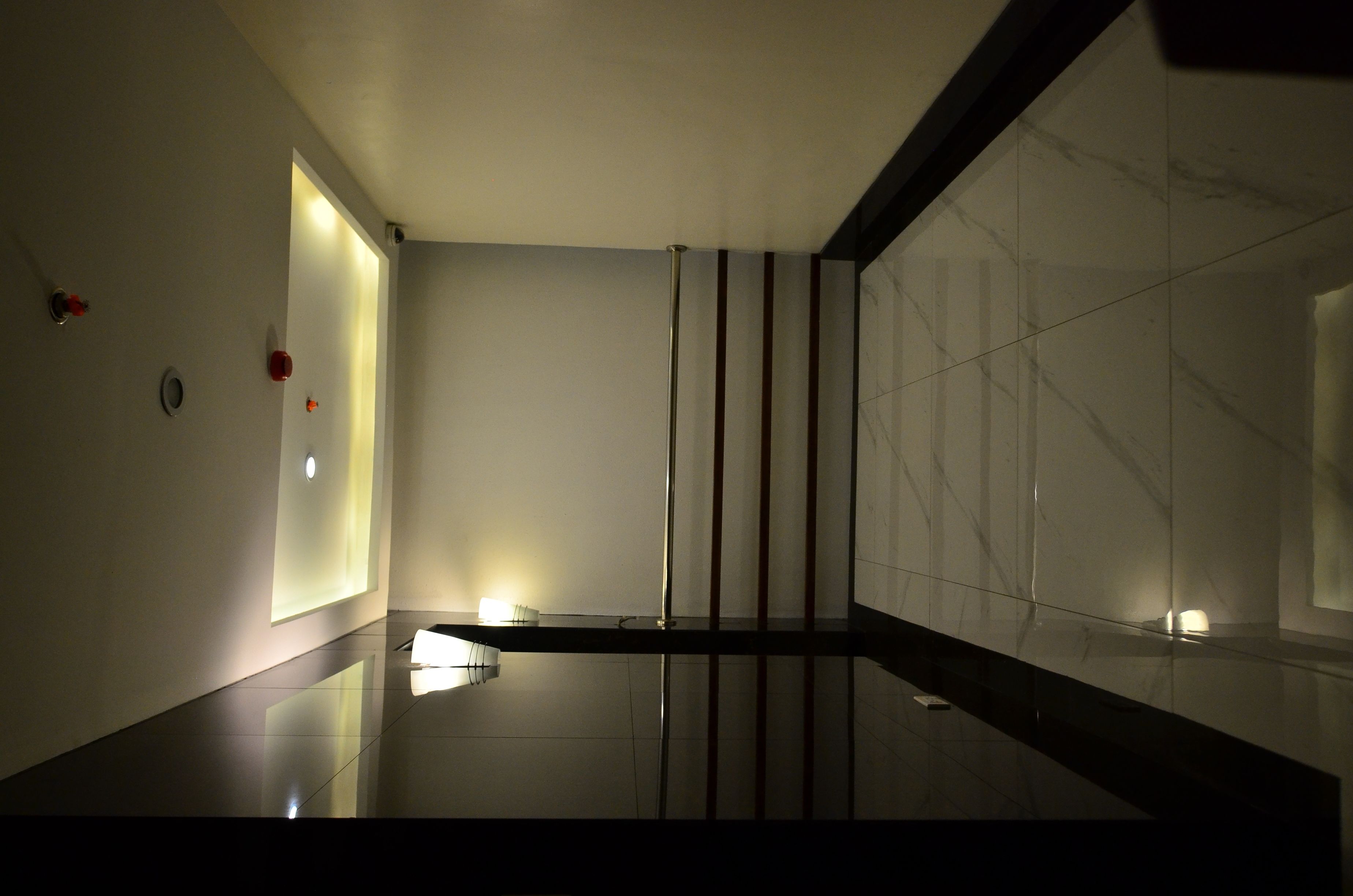 A modern, minimalist hallway with reflective flooring, a glass partition, and recessed lighting.