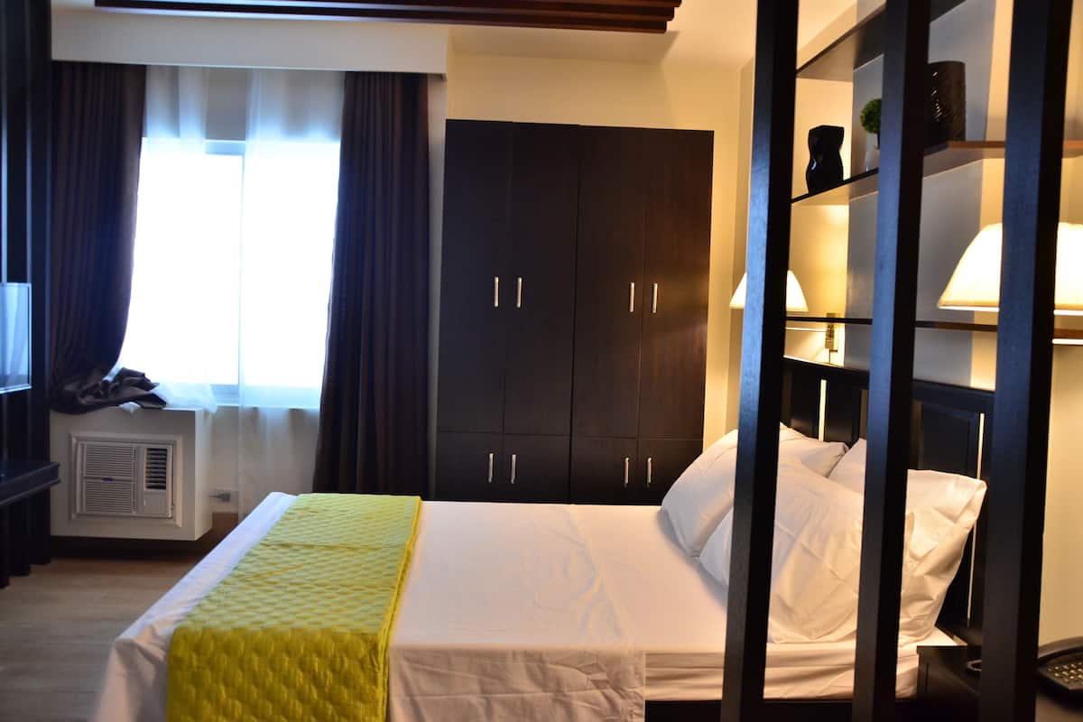 Une chambre d’hôtel avec un lit, une armoire, un bureau et une fenêtre avec des rideaux.