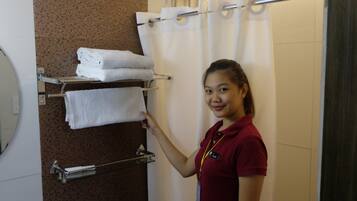 A person in a red uniform standing in a bathroom with a towel rack holding folded towels.