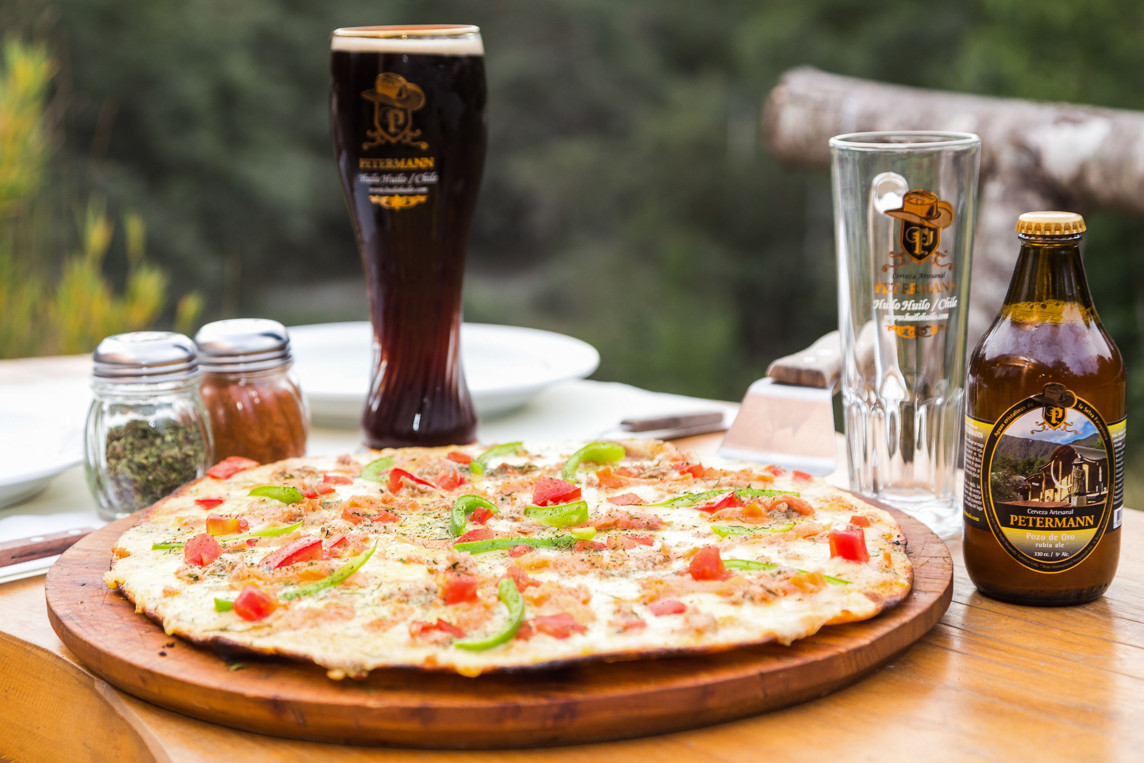 Pizza sobre una tabla de madera, con una botella de cerveza y vasos sobre la mesa.
