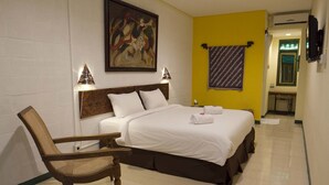 A hotel room with a bed, a wooden chair, a painting on the wall, and a towel on the bed. - SARE Suites (Jakarta)