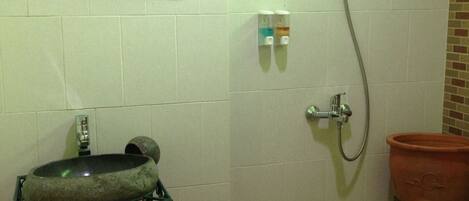 Un baño con un lavabo de piedra, un espejo, ducha y una pequeña maceta de terracota.