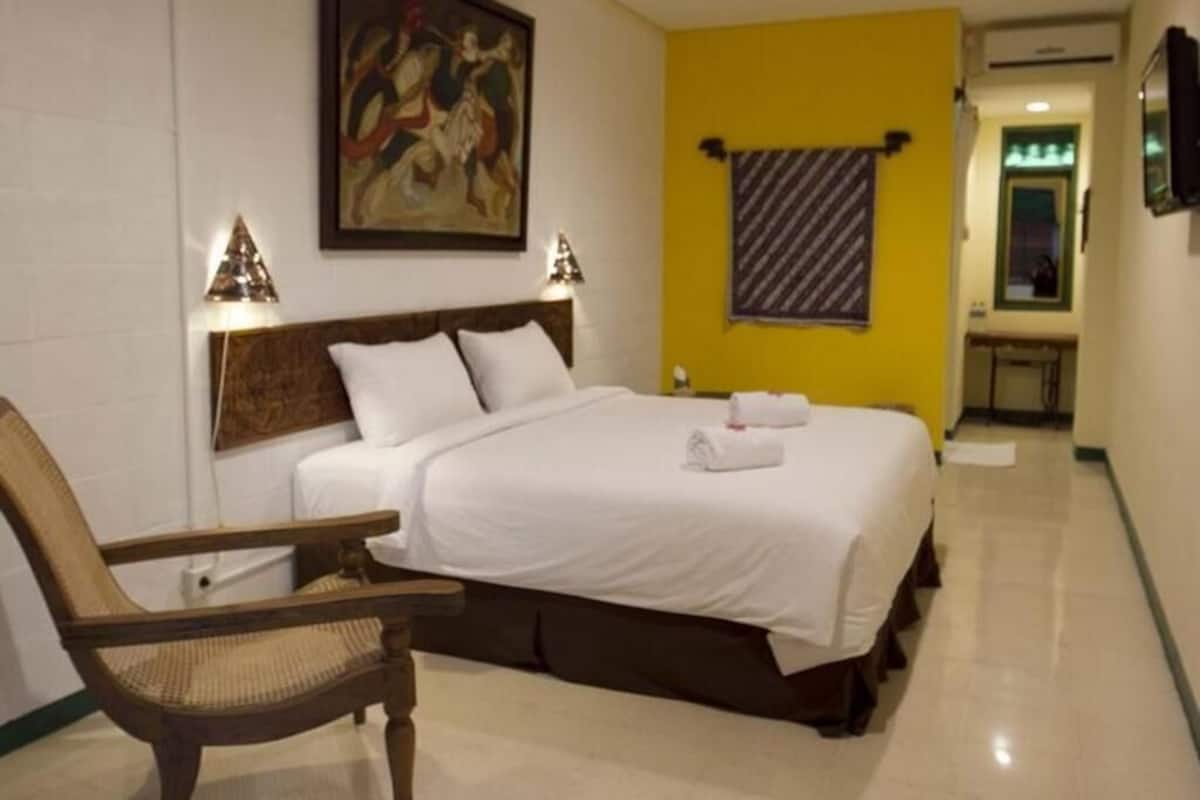 A hotel room with a bed, a chair, a painting on the wall, and a towel rack.