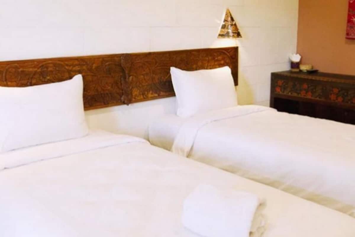 A hotel room with two beds, a wooden headboard, a nightstand, and a lamp.