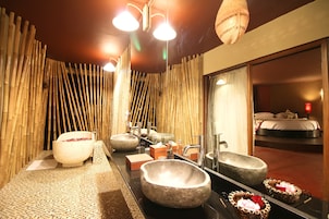 A modern bathroom with a large mirror, two stone sinks, and a bamboo wall.