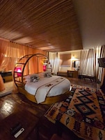 A cozy bedroom with a circular bed, wooden ceiling, and a patterned rug.