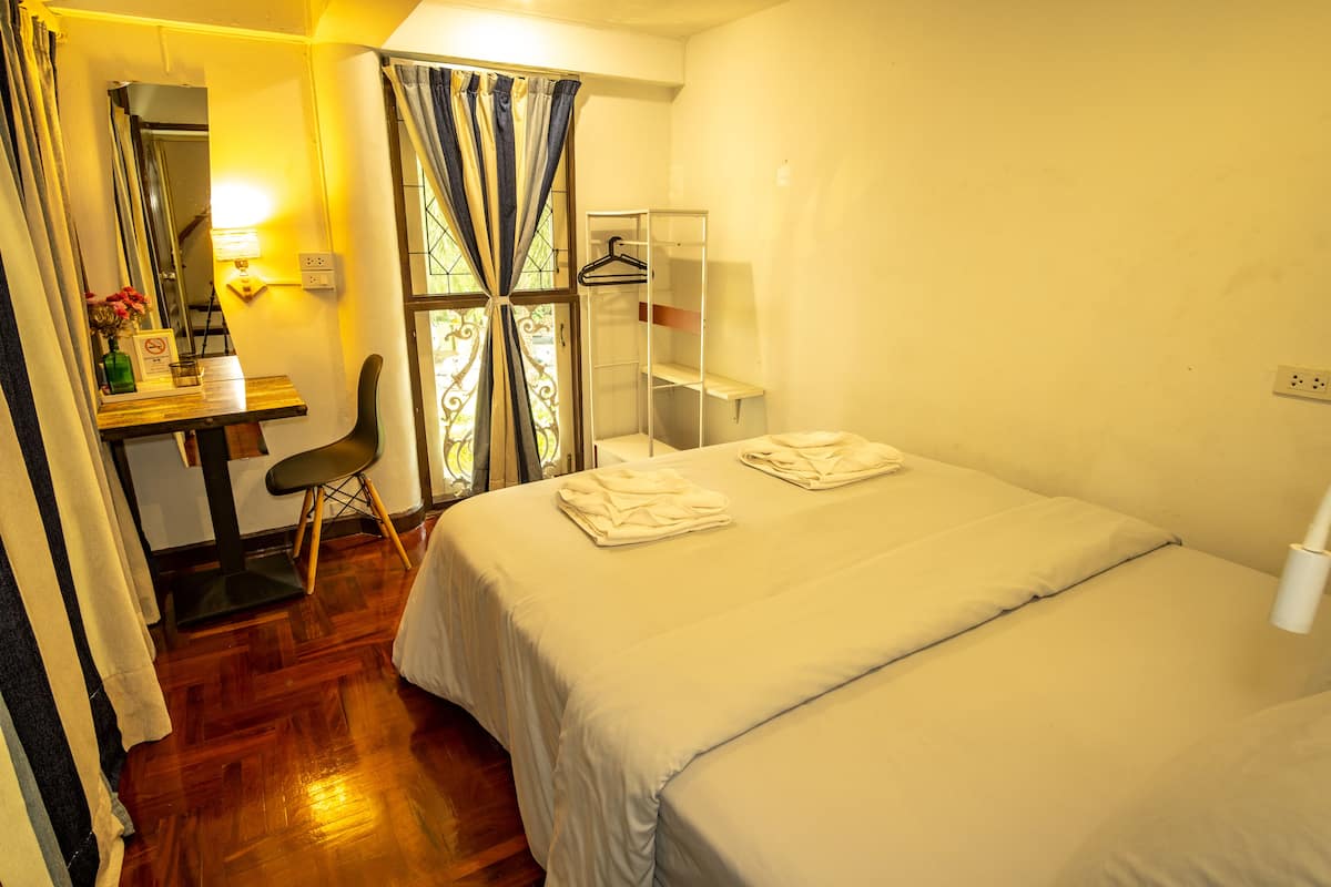 A bedroom with a bed, a desk, a chair, a mirror, and a window with curtains.