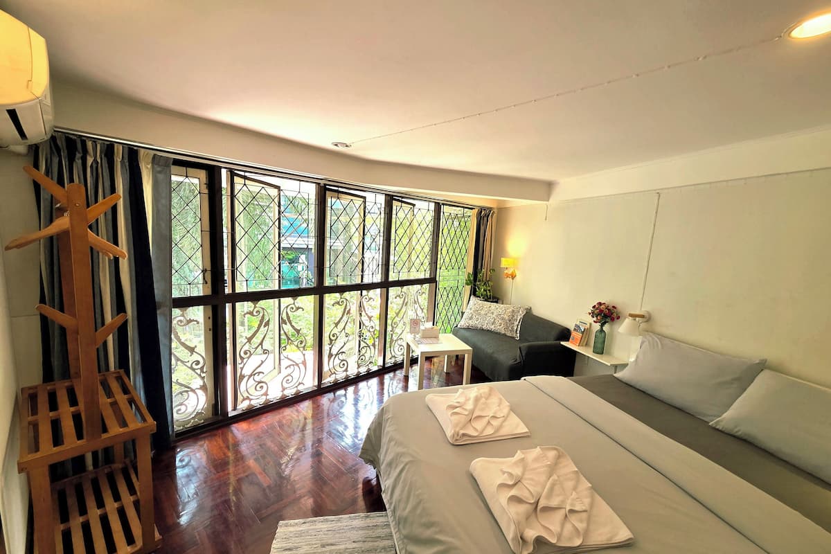 A modern hotel room with a large bed, a small desk, and a view through a large window.
