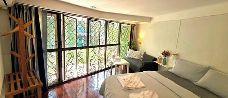 A modern hotel room with a large bed, a small desk, and a view through a large window.
