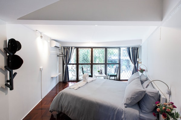 A modern bedroom with a large bed, a small table, and a view of the outdoors through large windows.