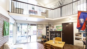A spacious room with a tiled floor, a wooden table, a sofa, and a balcony with a railing. - Home16 Hostel 16 (Bangkok)
