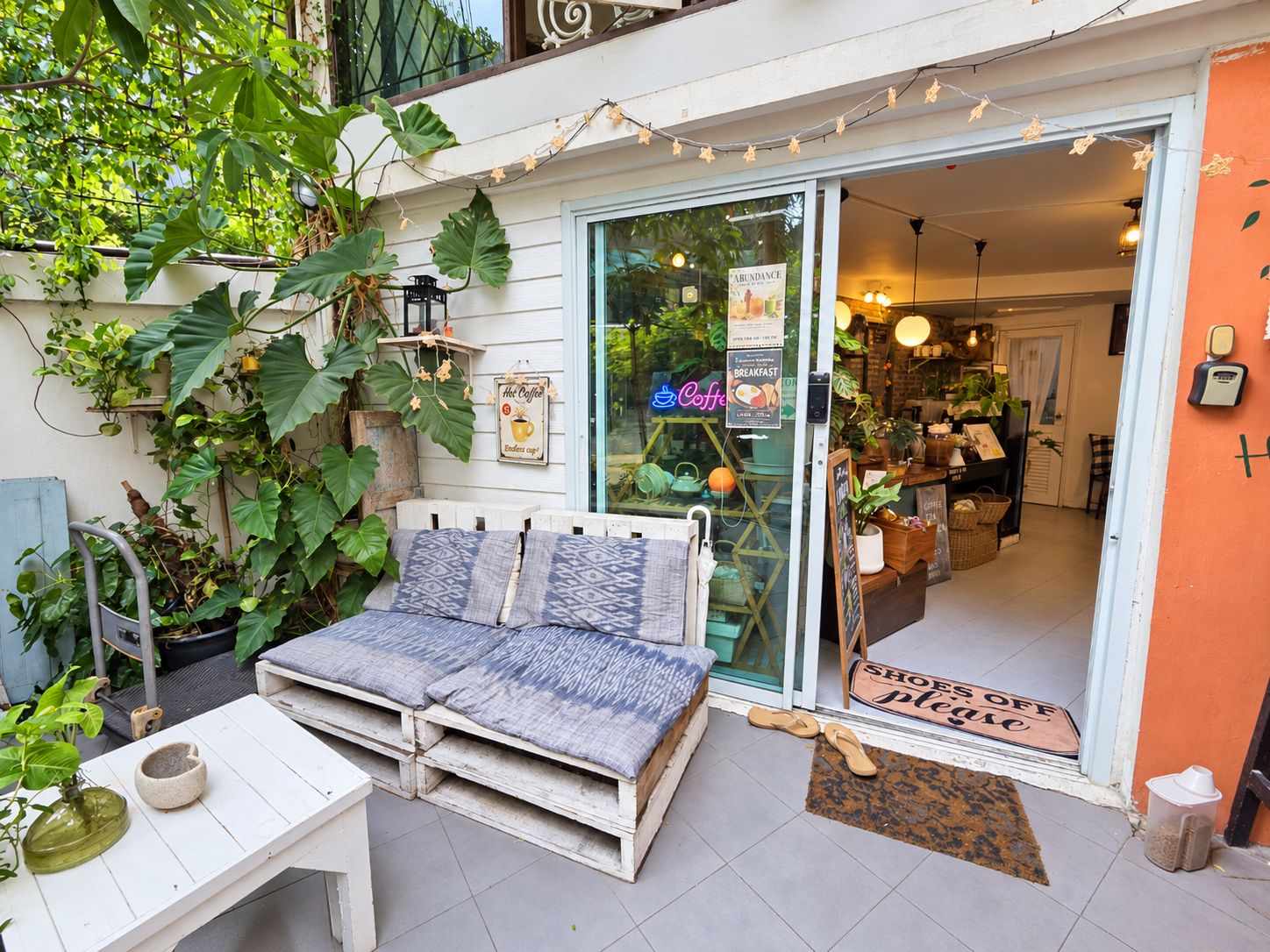 A cozy outdoor seating area with a wooden bench and a table, surrounded by lush greenery and plants.