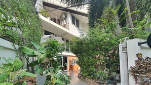 A narrow pathway flanked by lush greenery and a white building with a balcony. - Home16 Hostel 16 (Bangkok)