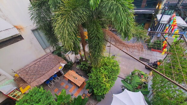 An outdoor patio area with a thatched roof table, potted plants, and a white umbrella. - Home16 Hostel 16 (Bangkok)