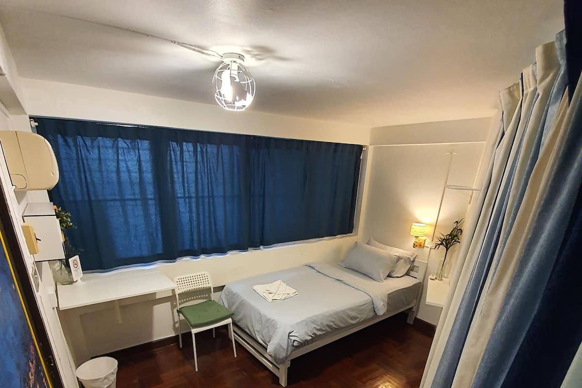 A room with a bed, bedside table, lamp, and a window with curtains.
