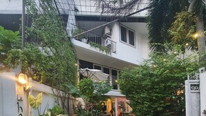A courtyard with potted plants, a pathway leading to a building entrance, and a white wall with a sign. - Home16 Hostel 16 (Bangkok)