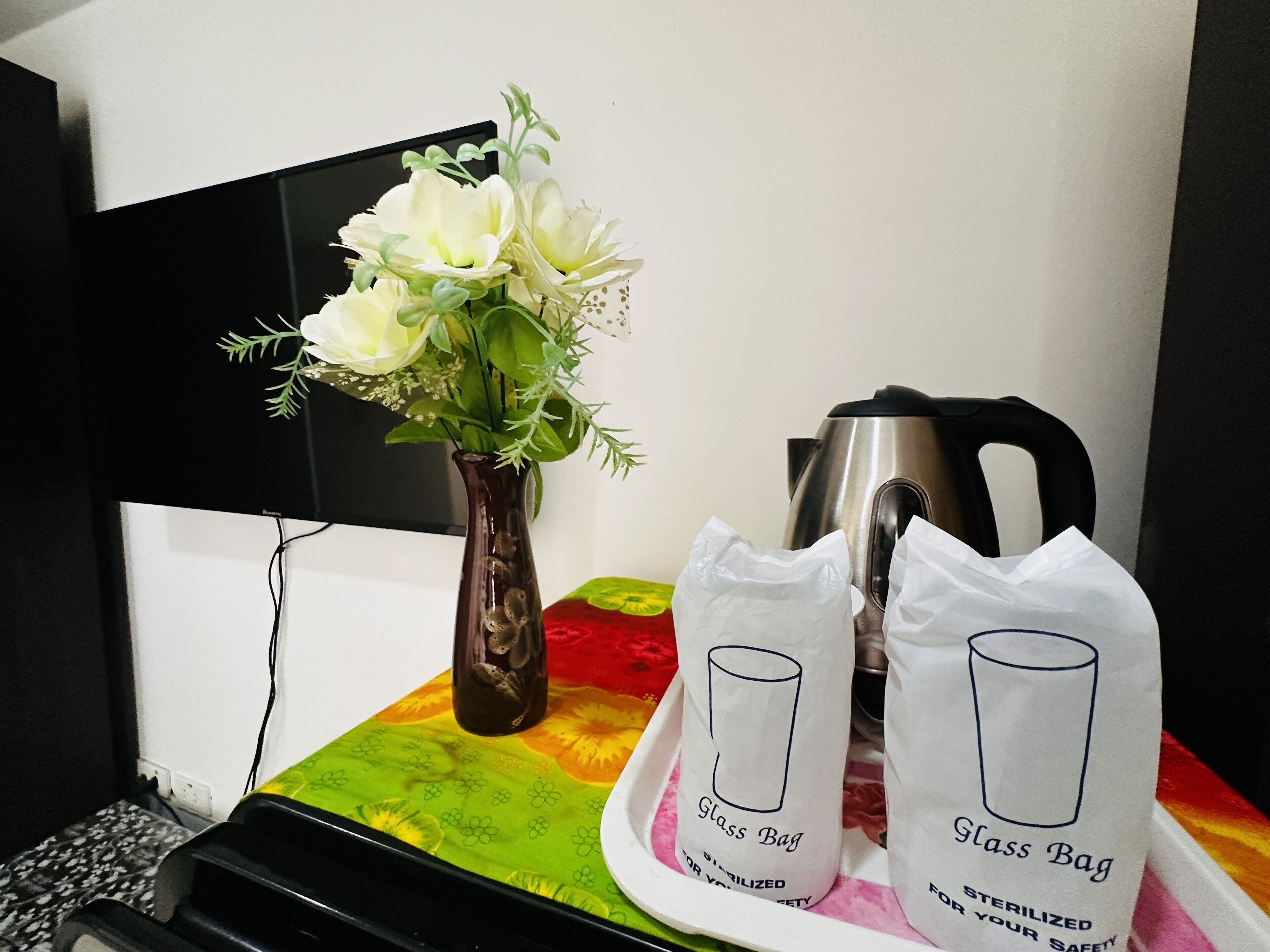 Un bureau avec un vase de fleurs, une bouilloire et deux paquets de thé en sachets.