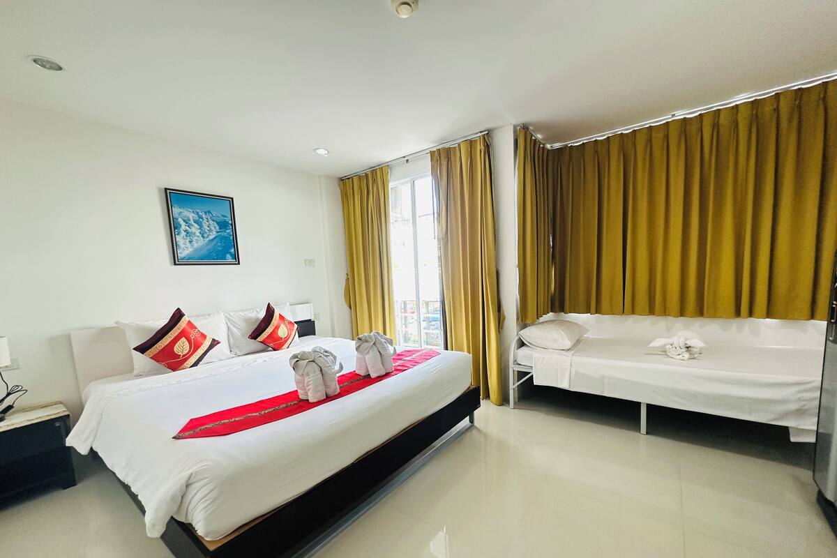 A hotel room with a large bed, a smaller bed, and a desk with a lamp.