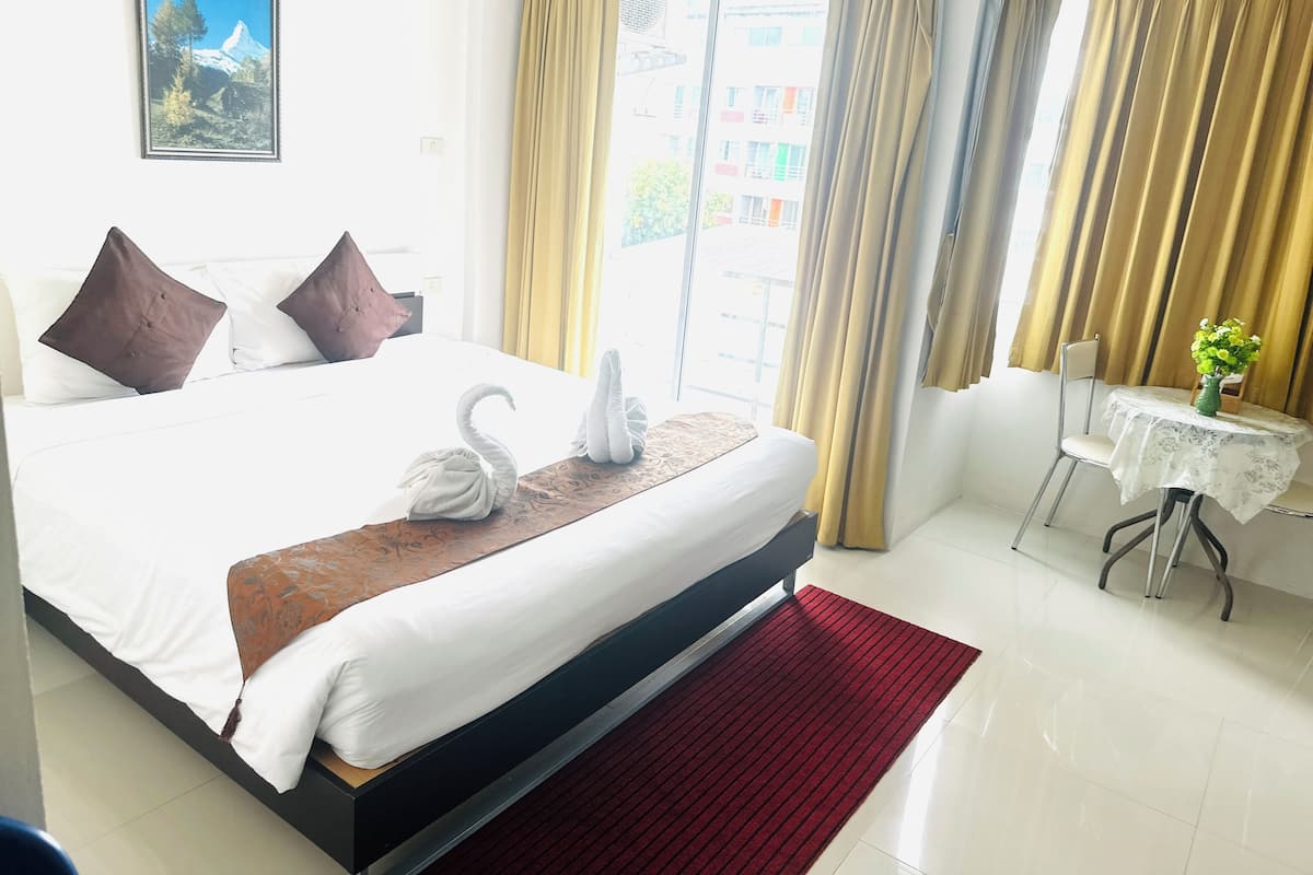 A hotel room with a large bed, a red rug, a desk with a chair, and a window with curtains.
