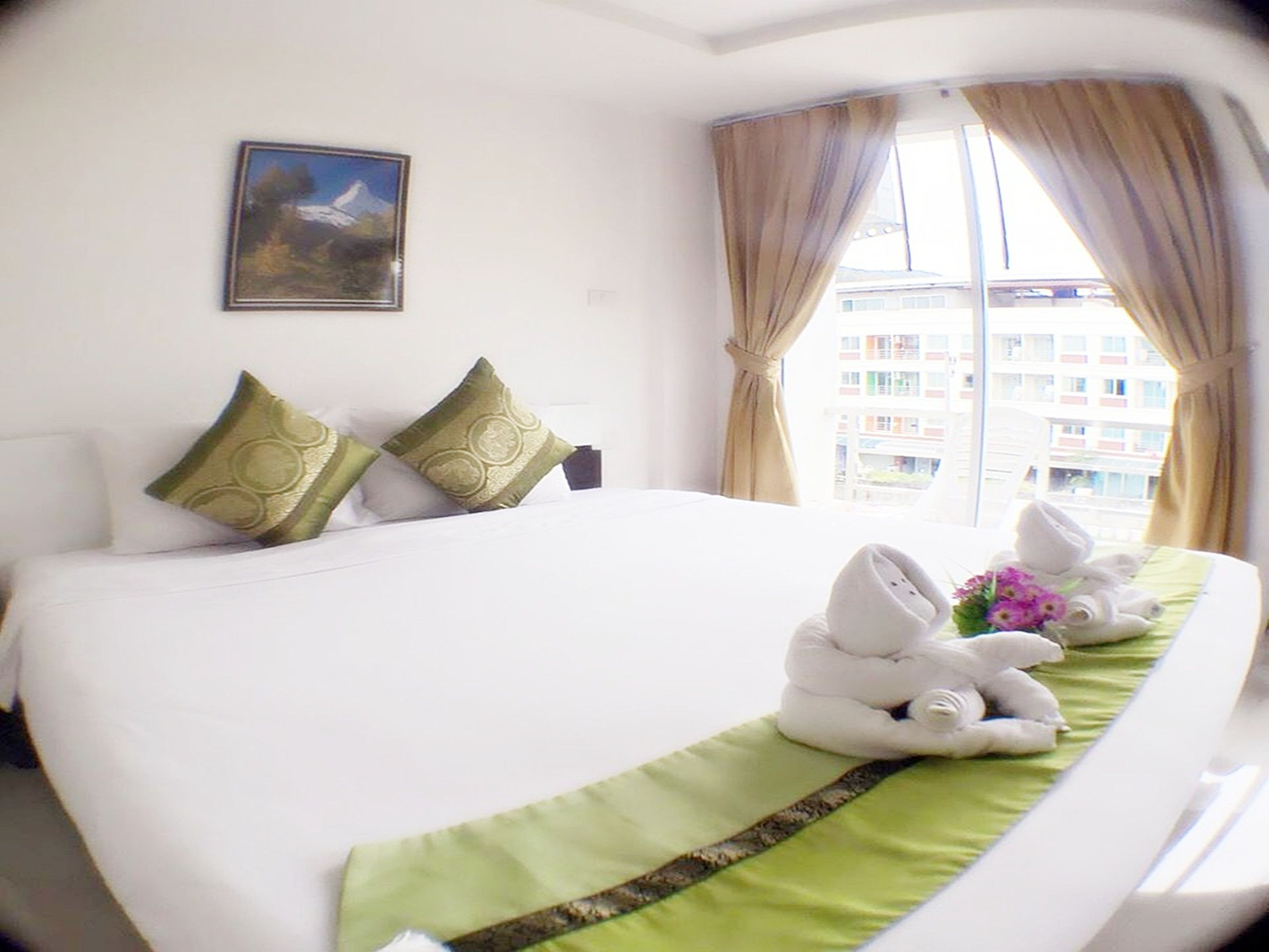A hotel room with a large bed, two pillows, a painting on the wall, and a window with curtains.