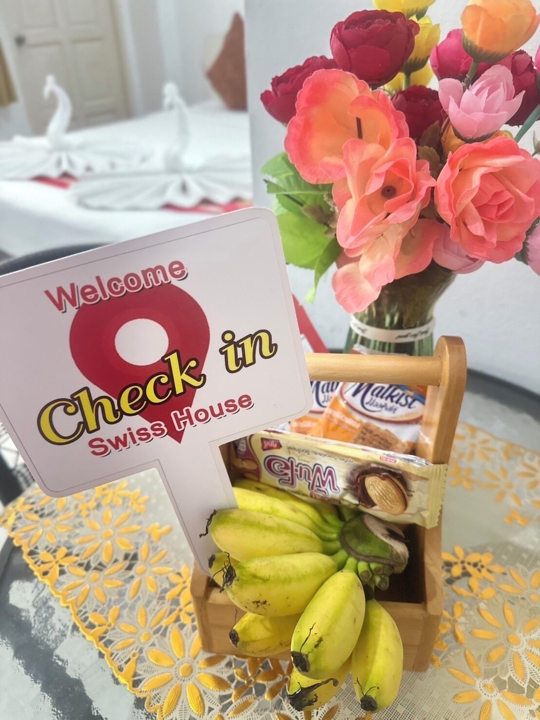 Une pancarte d’accueil ornée d’un cygne, un bouquet de fleurs et une boîte de bananes.