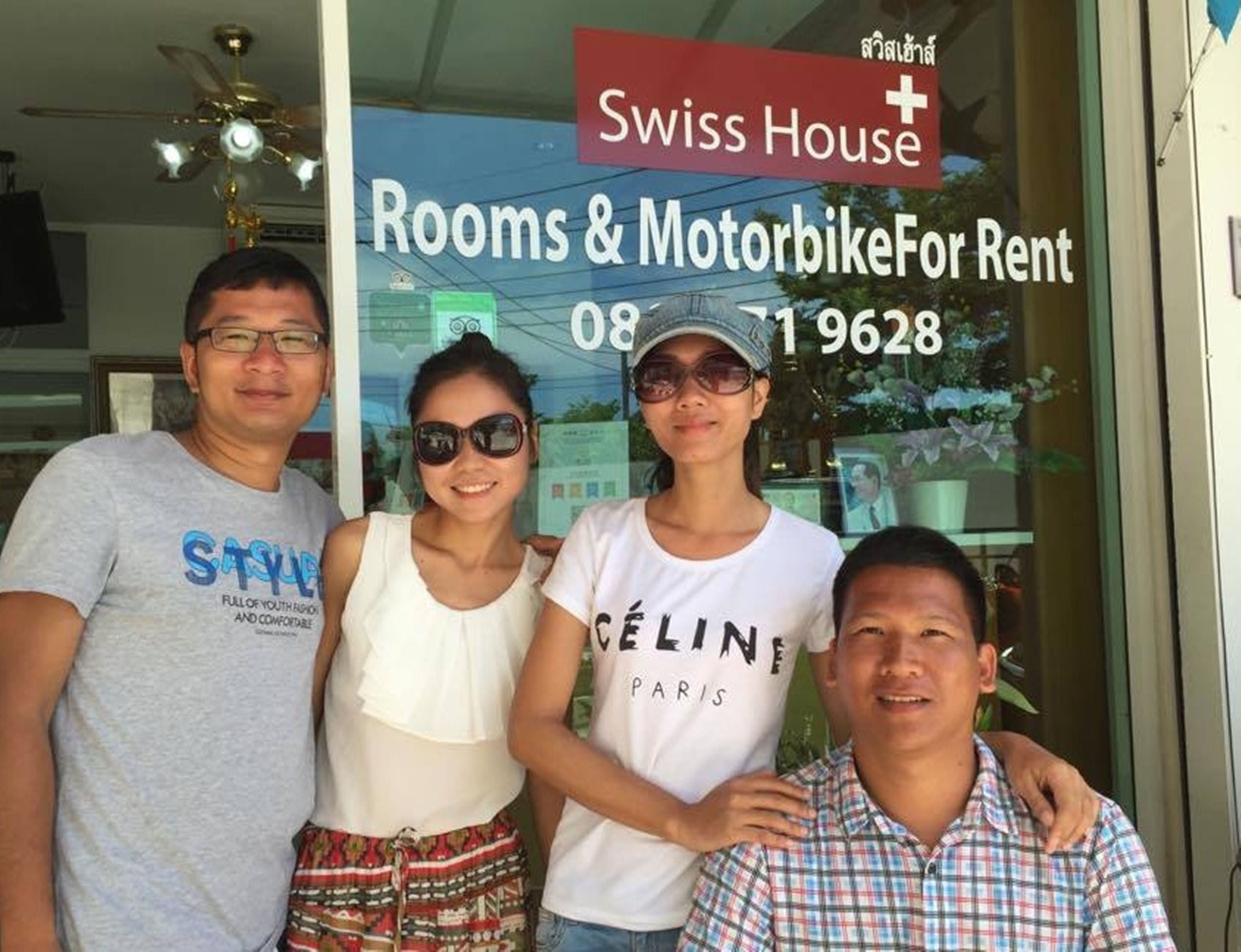 A group of people standing in front of a sign for Swiss House, which advertises rooms and motorbike rentals.