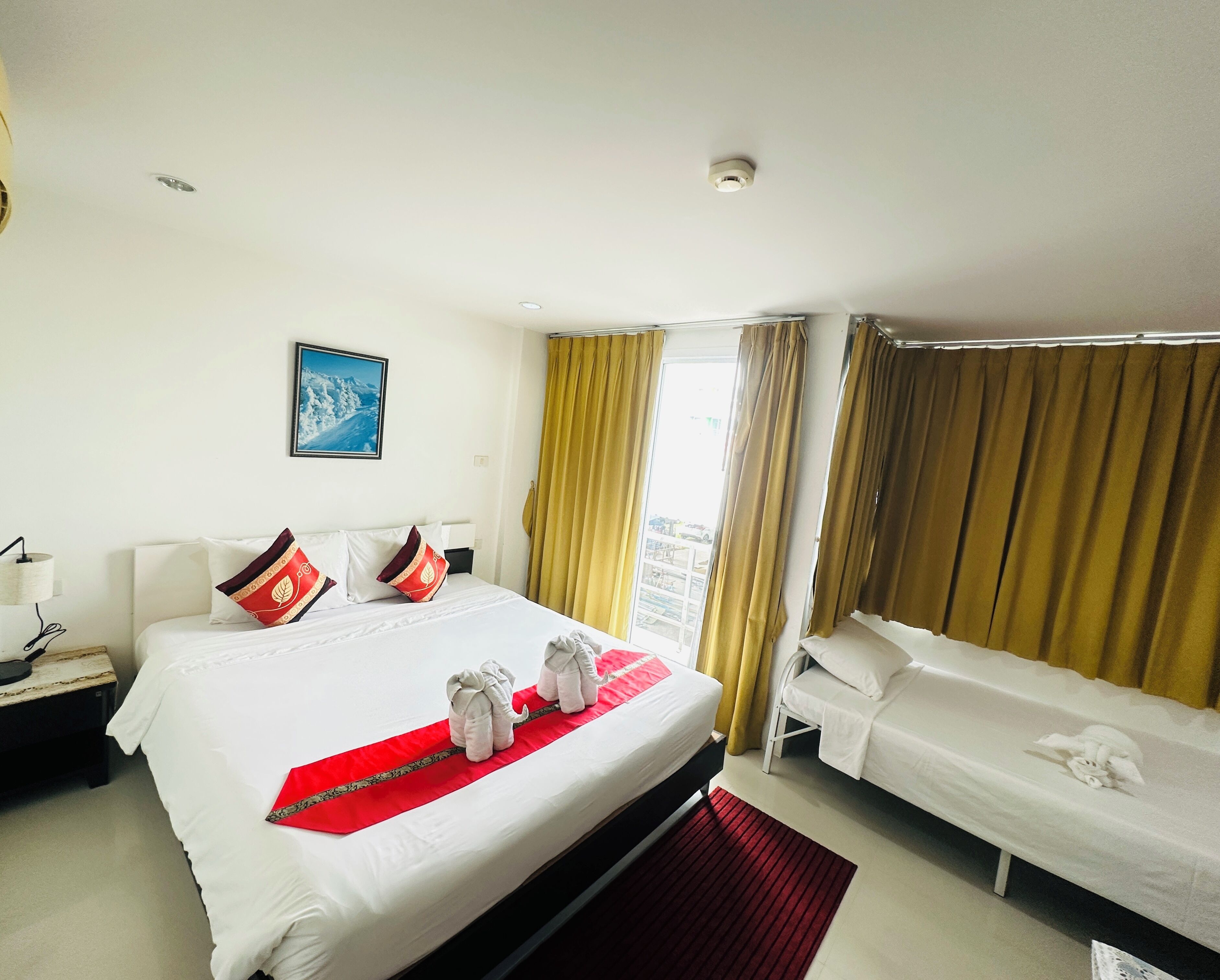 A hotel room with a large bed, two smaller beds, a nightstand, a lamp, a painting on the wall, and a window with curtains.