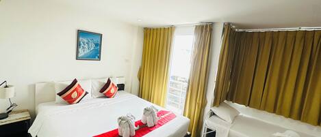 A hotel room with a large bed, two smaller beds, a nightstand, a lamp, a painting on the wall, and a window with curtains.
