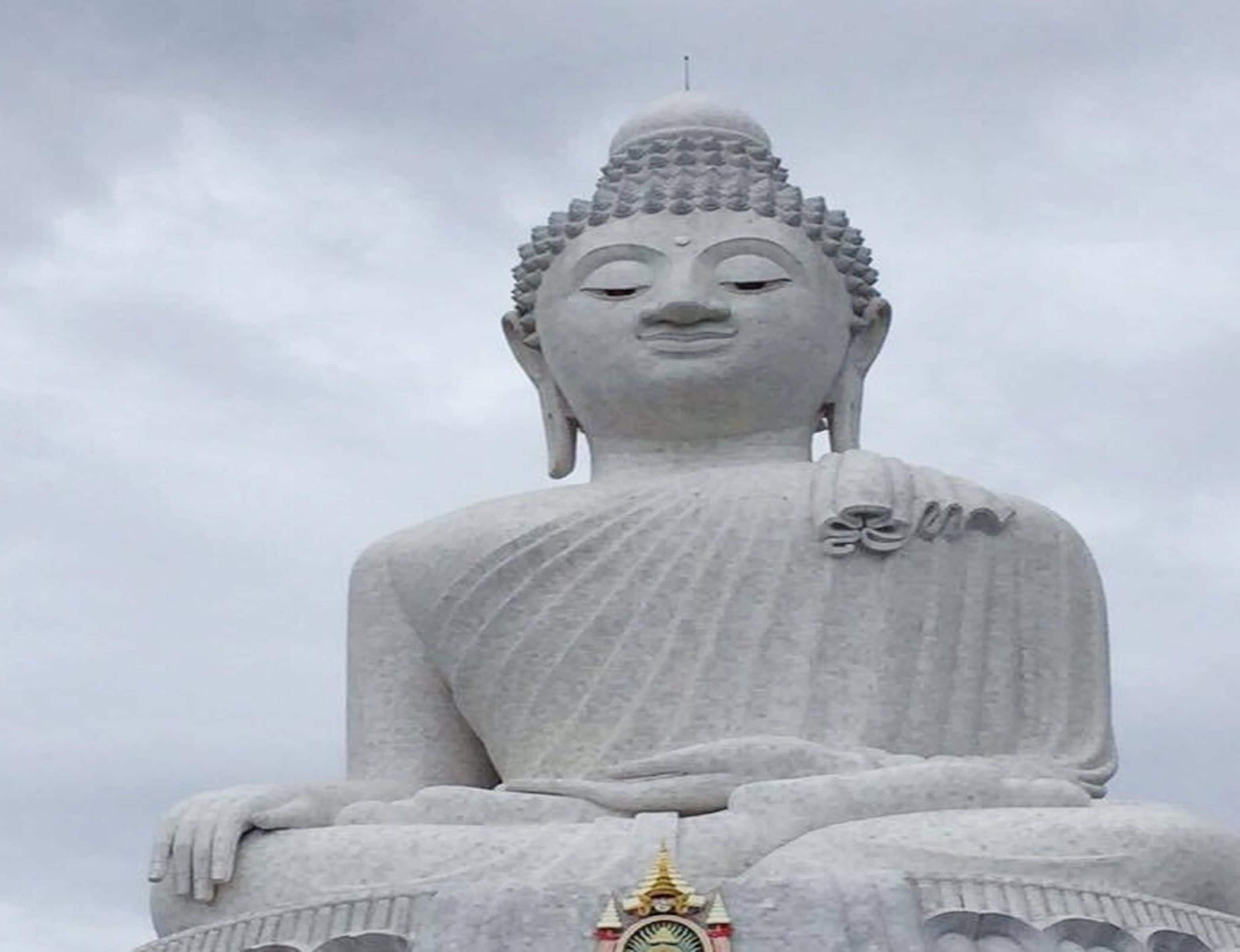 Une grande statue de Bouddha assis, surmontée d’un élément décoratif doré.